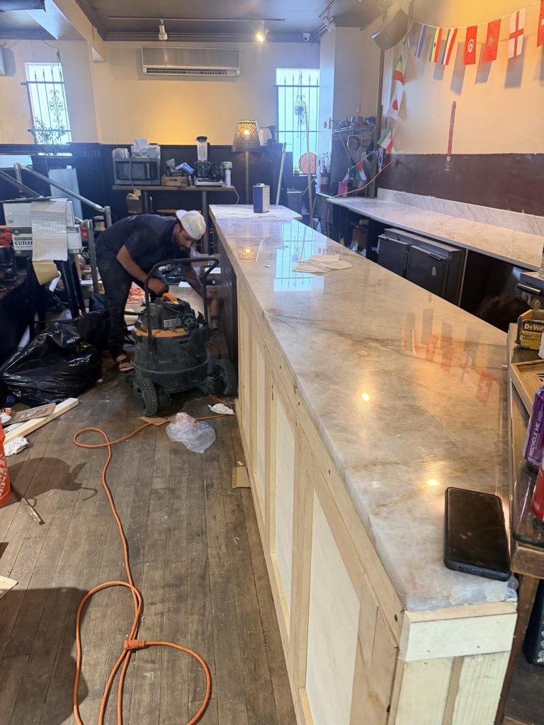 - 6 Installer setting the Patagonia quartzite slab onto the lit counter base at Luxor Cafe